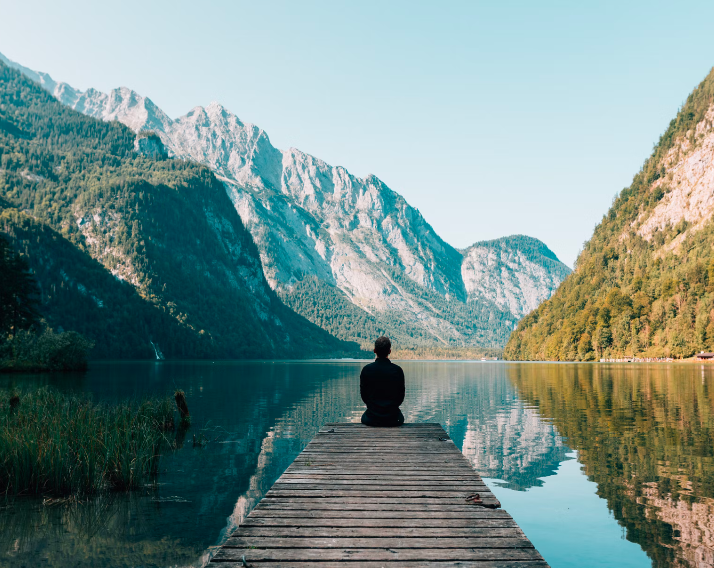Person sitting at end of dock overlooking mountain range and lake