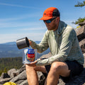 Man pours water into a Korean-Inspired Beef pouch while seated on a rocky mountainside.