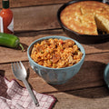 Bowl of jambalaya with cornbread and hot sauce on a wooden table