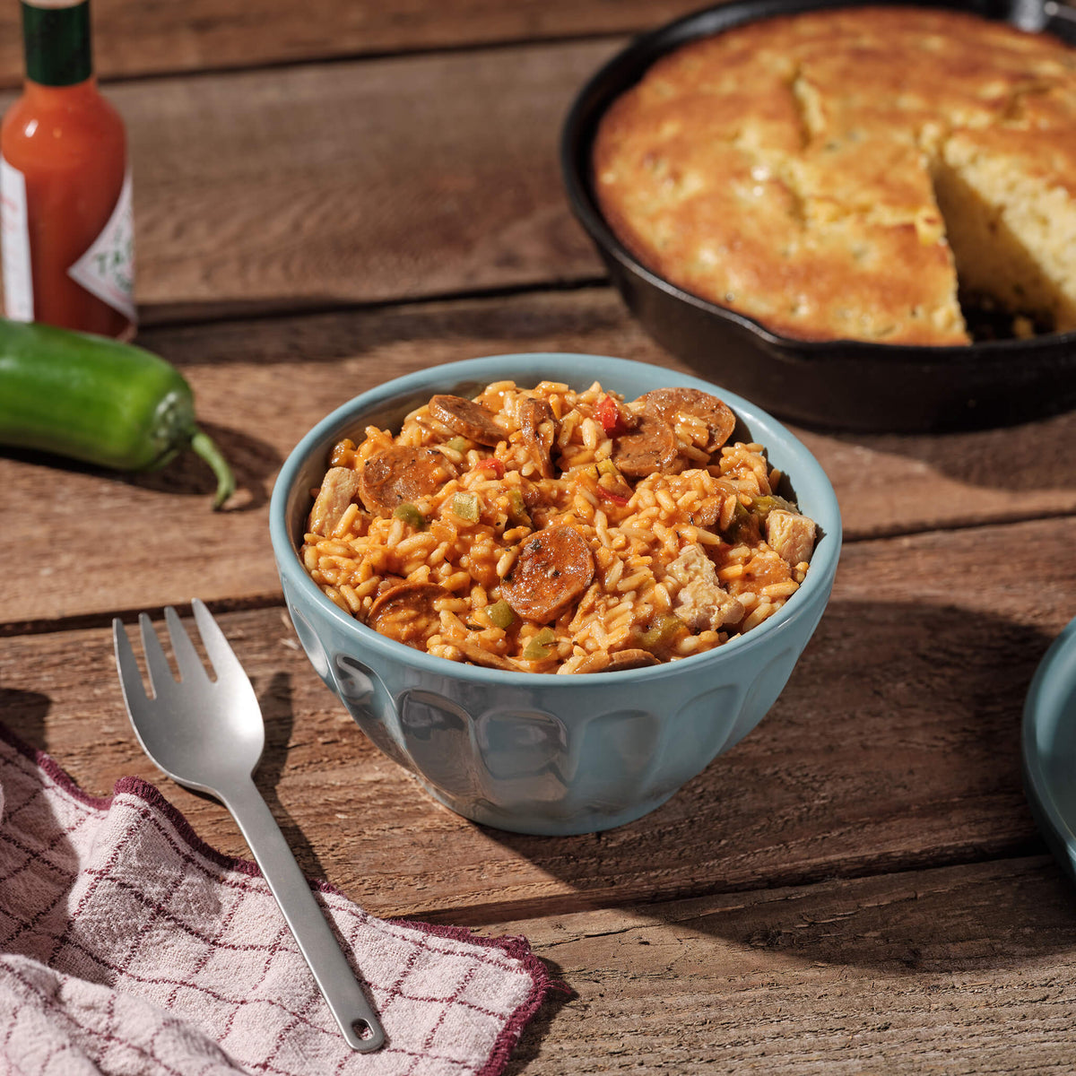 Bowl of jambalaya with cornbread and hot sauce on a wooden table