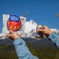 Person holds a Rainier beer and Mountain House Pizza Bowl in front of Mount Rainier.