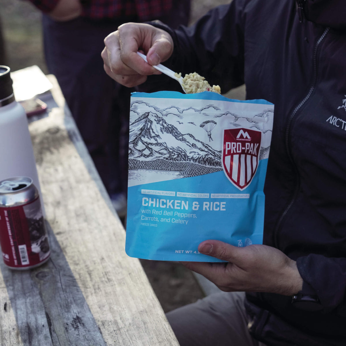 Person sitting at a picnic table scooping out a spoonful of Mountain House Chicken & Rice Pro-Pak.