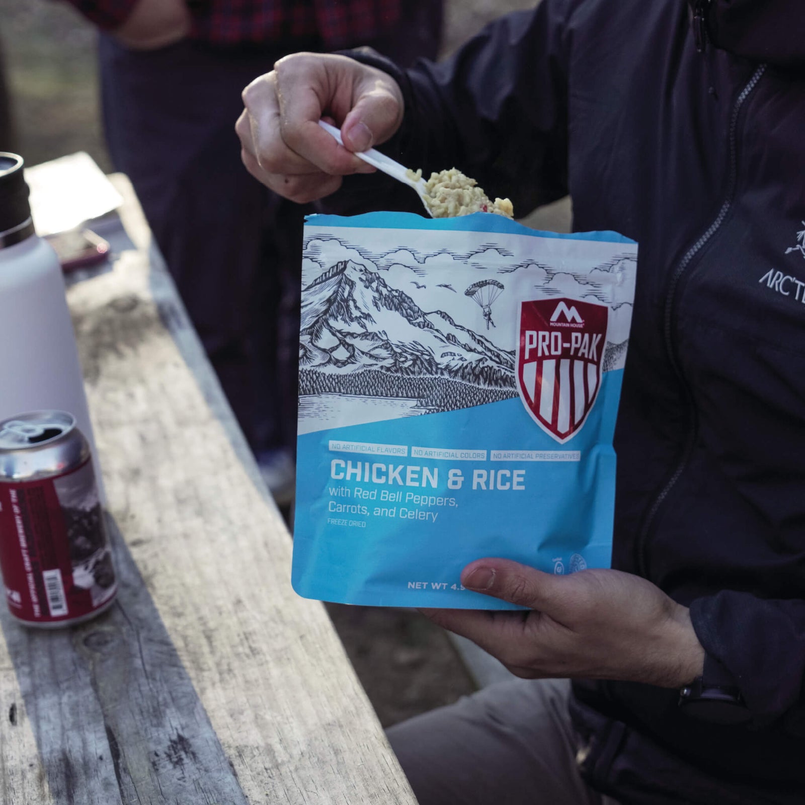 Person sitting at a picnic table scooping out a spoonful of Mountain House Chicken & Rice Pro-Pak.