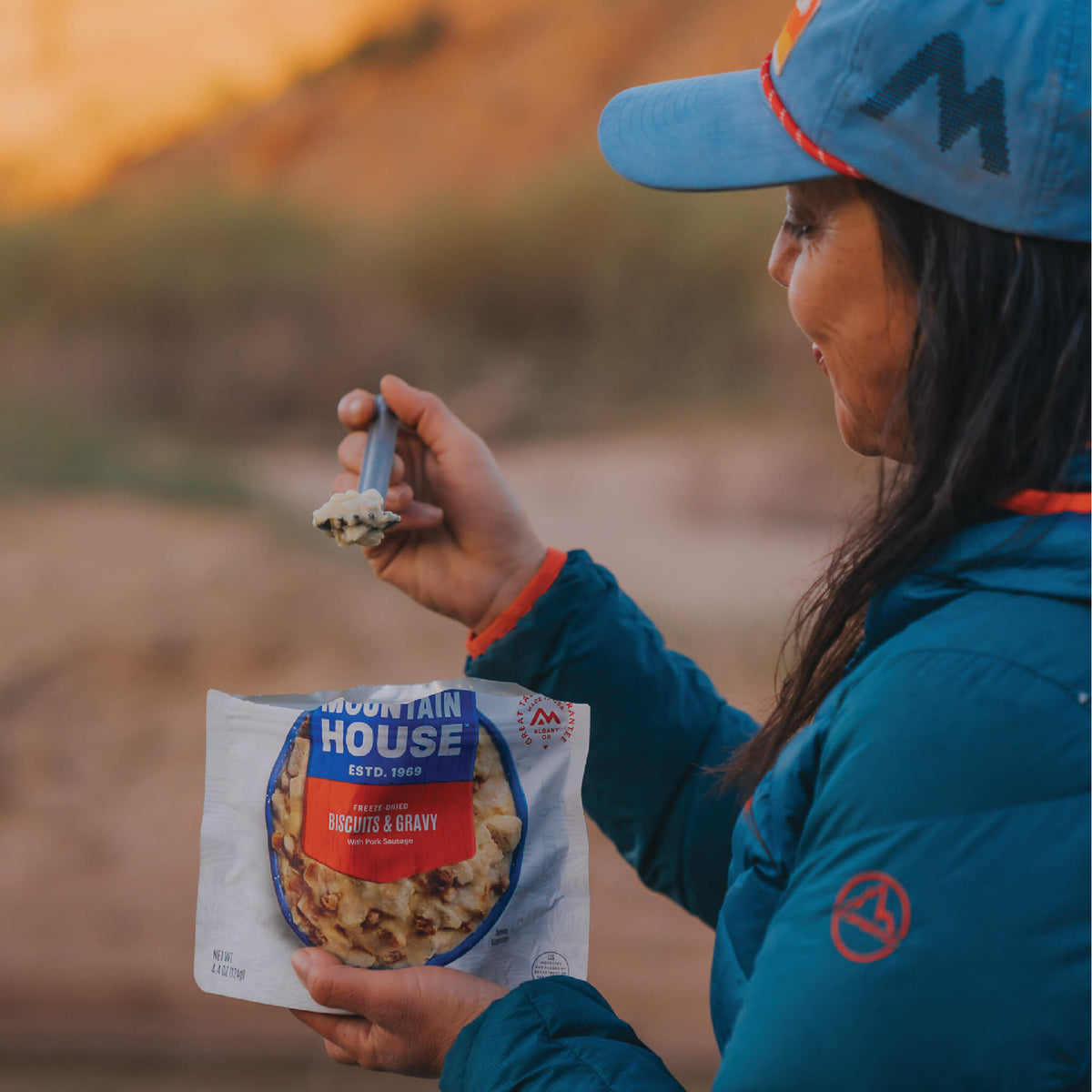 Person in the backcountry looking at a spoonful of Mountain House Biscuits & Gravy and smiling.