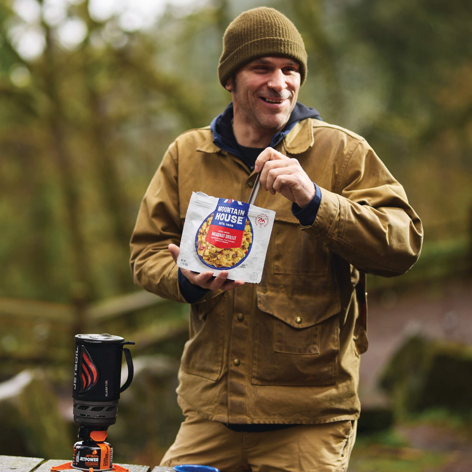 Man standing by a picnic table eating from a Mountain House Breakfast Skillet pouch in a campground