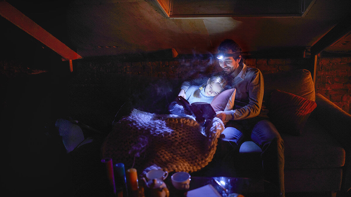 Dad reading to daughter during a power outage with headlamps.