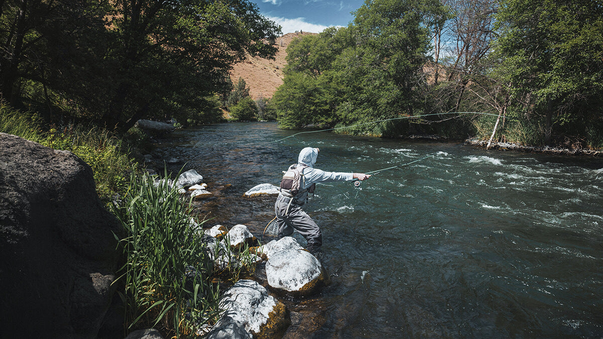 Person fly fishing in a river surrounded by trees and rocks.
