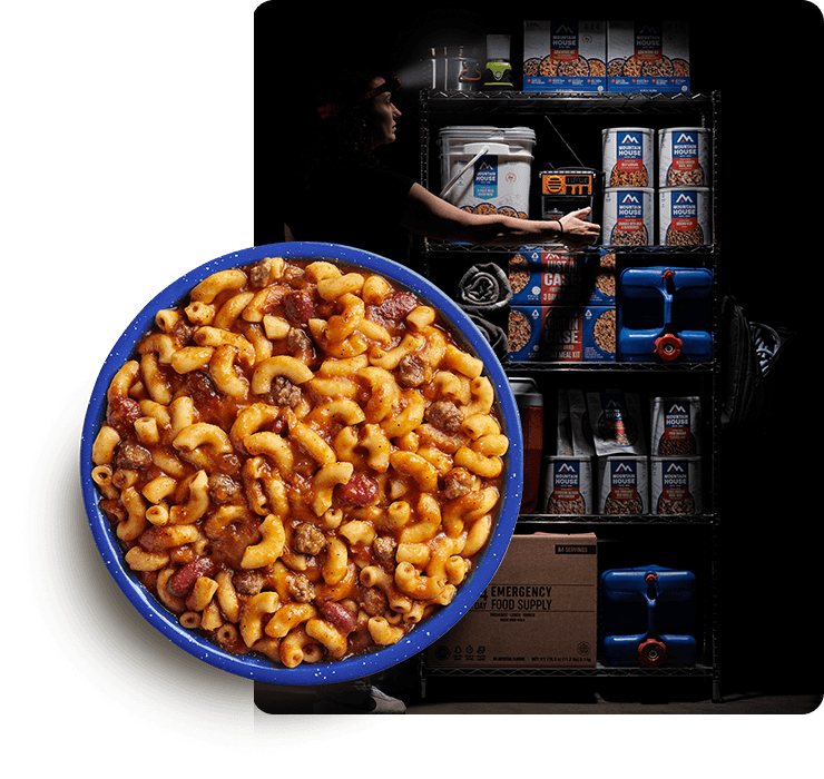 Person wearing a headlamp gathers emergency supplies during a power outage with a bowl of Mountain House Chili Mac in the foreground.