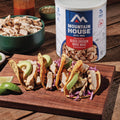 Mountain House Freeze-Dried Grilled Chicken on a wood countertop with tacos and hot sauce.